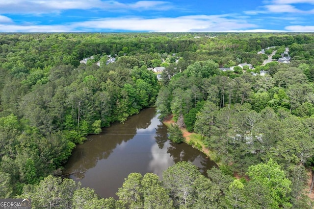aerial view of property and surrounding area with a heavily wooded area and a nearby body of water