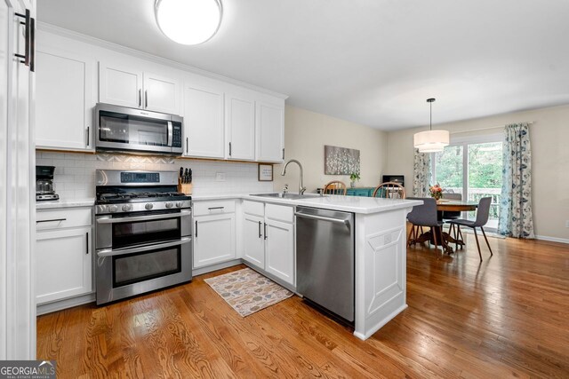 164 Stoneforest Dr, Woodstock, GA 30189 - kitchen featuring stainless steel appliances, a peninsula, backsplash, light countertops, and light wood-style flooring