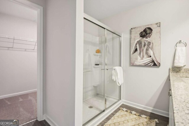 bathroom with a shower stall, a spacious closet, baseboards, vanity, and wood finished floors