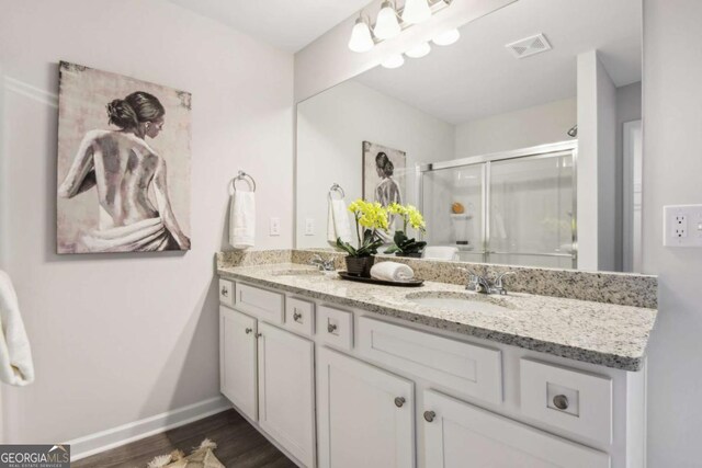 bathroom with a shower stall, double vanity, wood finished floors, and baseboards