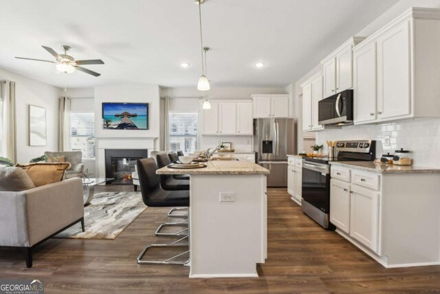 kitchen featuring appliances with stainless steel finishes, open floor plan, a glass covered fireplace, white cabinetry, and recessed lighting