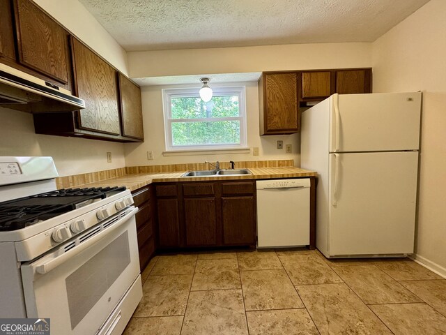 kitchen with white appliances, a sink, under cabinet range hood, dark brown cabinets, and a textured ceiling