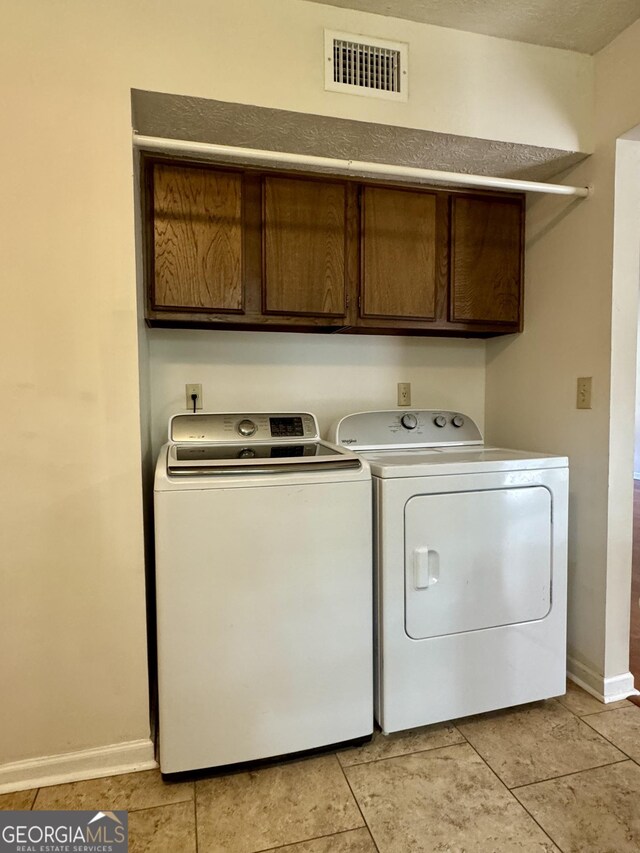 washroom featuring washing machine and clothes dryer, cabinet space, baseboards, and light tile patterned floors