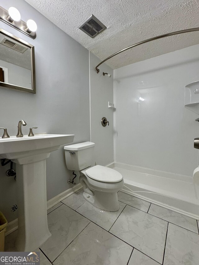 bathroom with marble look tile flooring, a shower, toilet, and a textured ceiling