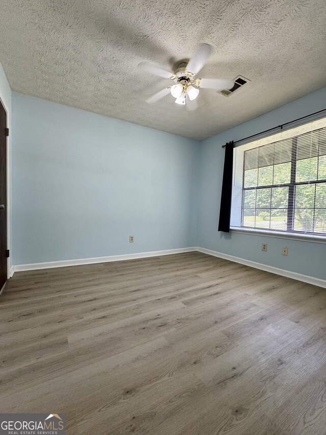 empty room featuring ceiling fan, baseboards, wood finished floors, and a textured ceiling