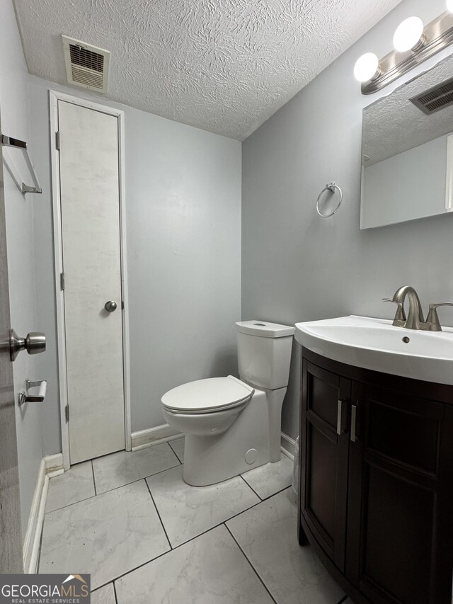 half bathroom with marble look tiles, toilet, vanity, a textured ceiling, and baseboards