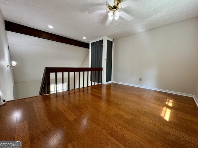 unfurnished room featuring a ceiling fan, wood finished floors, a textured ceiling, beamed ceiling, and baseboards