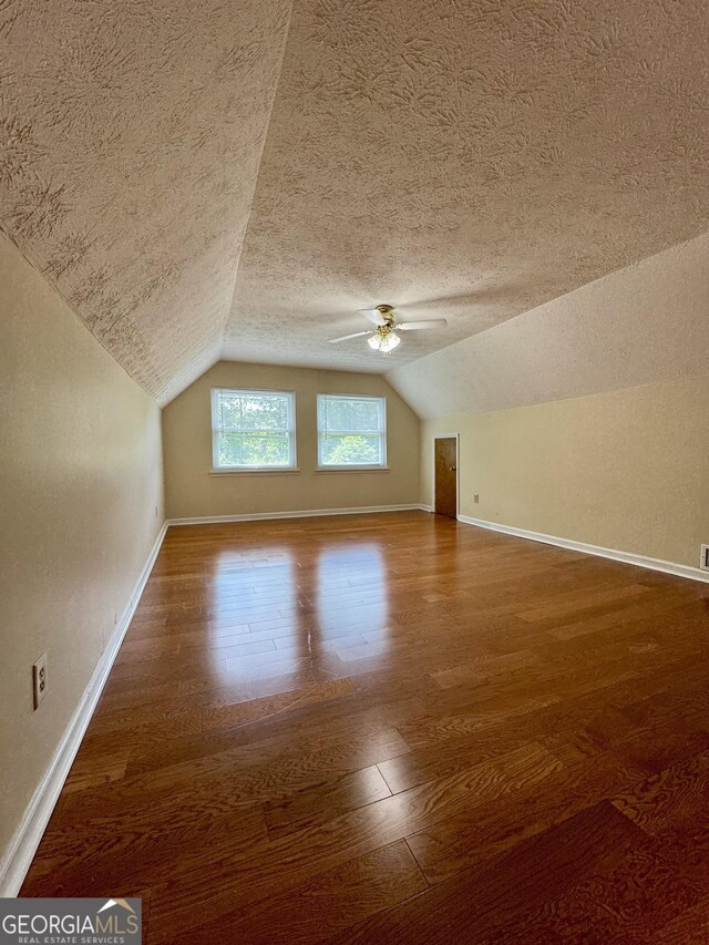 bonus room with a textured ceiling, vaulted ceiling, wood finished floors, baseboards, and a ceiling fan