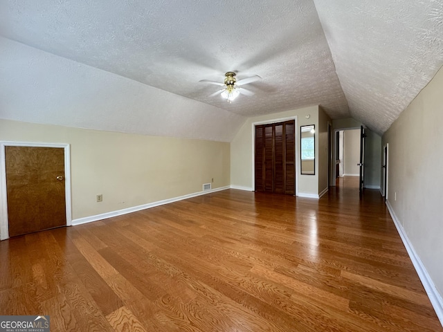 bonus room with a textured ceiling, wood finished floors, lofted ceiling, a ceiling fan, and baseboards