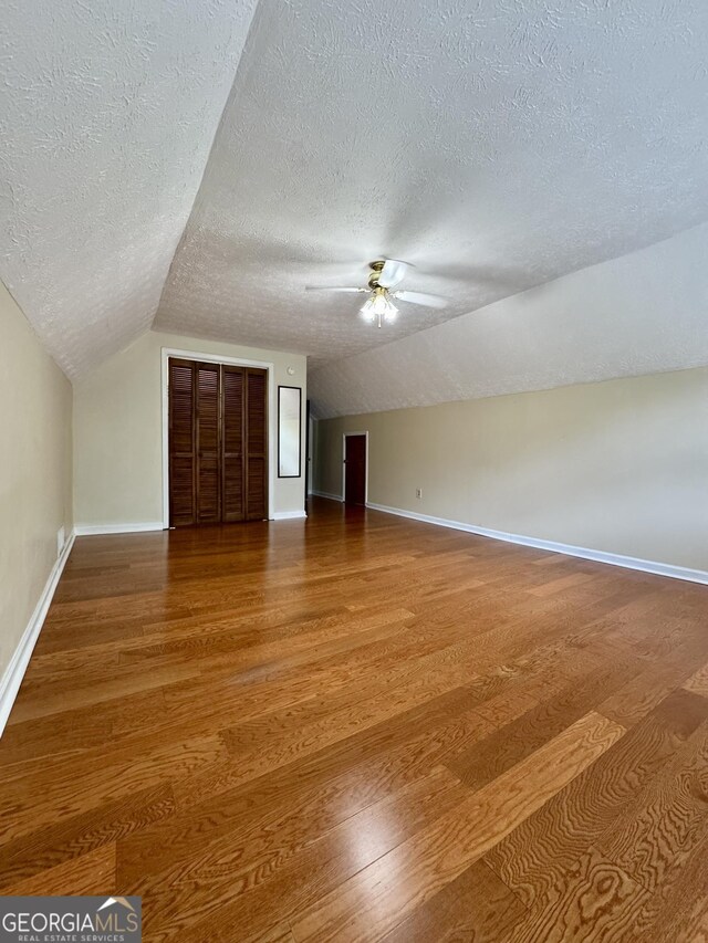 bonus room featuring a textured ceiling, vaulted ceiling, wood finished floors, ceiling fan, and baseboards