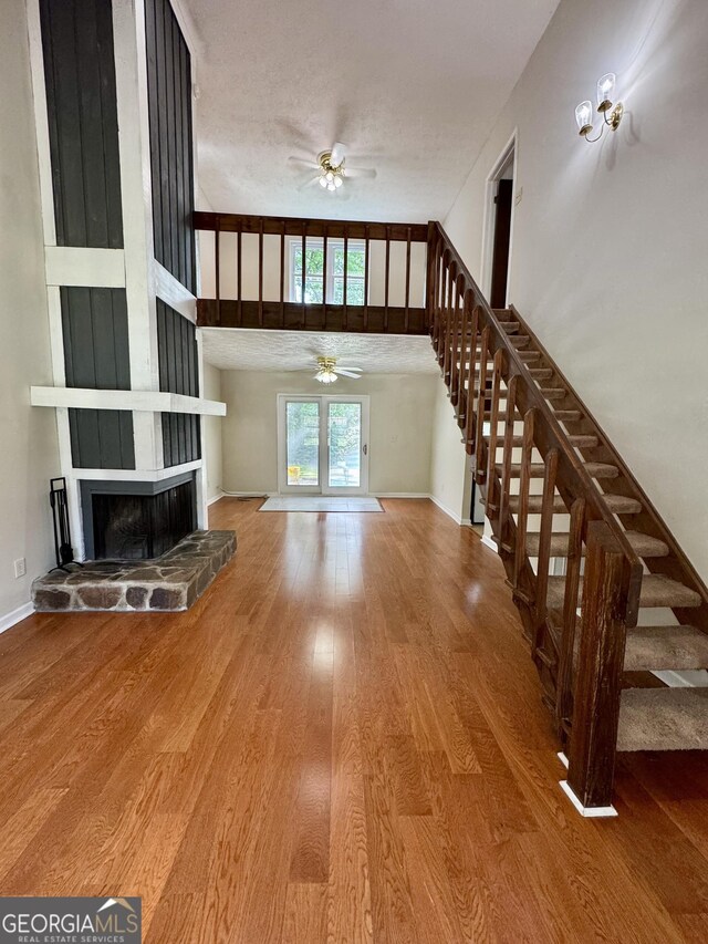 unfurnished living room featuring ceiling fan, stairs, wood finished floors, a fireplace, and baseboards