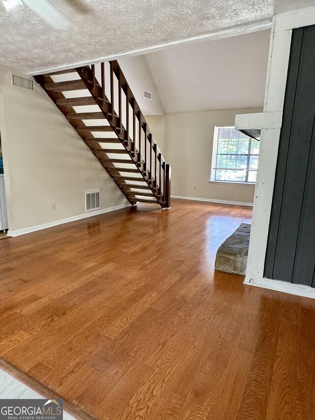 unfurnished living room with wood finished floors, baseboards, a textured ceiling, vaulted ceiling, and stairs