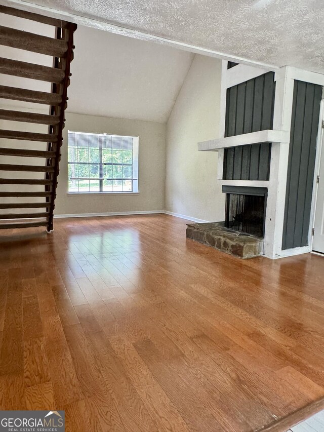 unfurnished living room with wood finished floors, a textured ceiling, vaulted ceiling, a large fireplace, and baseboards