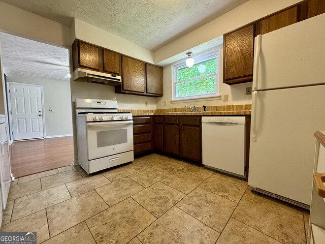 kitchen featuring white appliances, under cabinet range hood, a textured ceiling, light tile patterned floors, and dark brown cabinets
