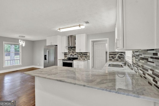 kitchen with appliances with stainless steel finishes, a sink, wall chimney range hood, backsplash, and white cabinets