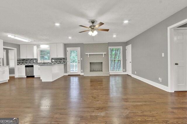 unfurnished living room featuring a ceiling fan, a textured ceiling, dark wood finished floors, a fireplace, and a sink