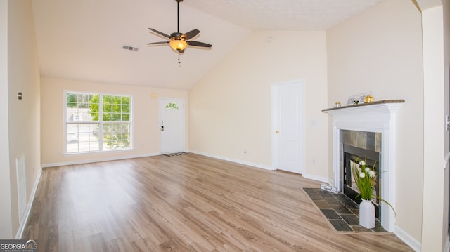 unfurnished living room featuring a tile fireplace, a ceiling fan, wood finished floors, baseboards, and high vaulted ceiling