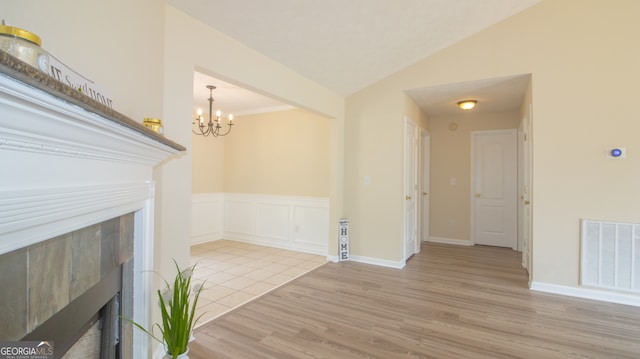 unfurnished living room with a tiled fireplace, wood finished floors, a chandelier, wainscoting, and lofted ceiling