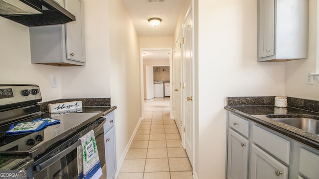kitchen featuring electric range, under cabinet range hood, light tile patterned flooring, washer / clothes dryer, and dark stone countertops