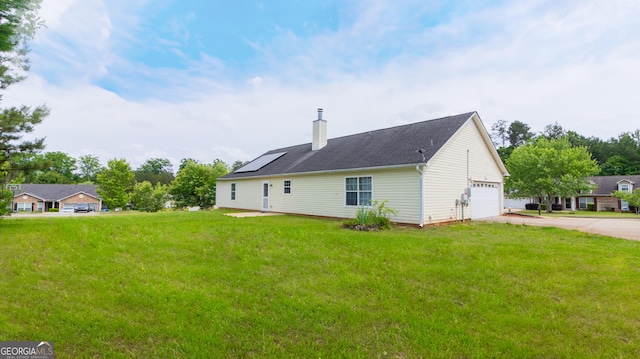 back of property featuring driveway, a chimney, a yard, and solar panels
