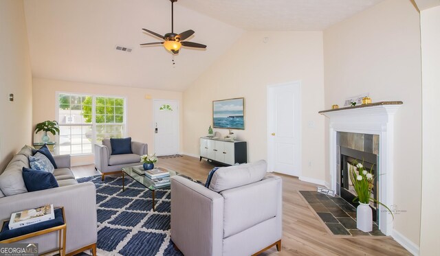 living area with wood finished floors, a fireplace, a ceiling fan, high vaulted ceiling, and baseboards