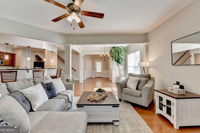 2505 Thackery Ct, Cumming, GA 30041 - living room featuring a ceiling fan, a chandelier, light wood finished floors, ornate columns, and stairs