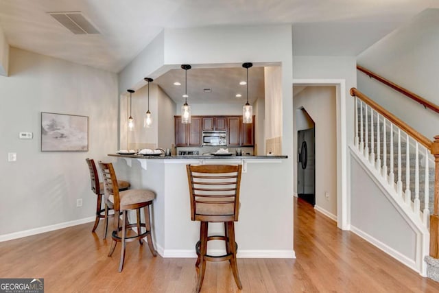 2505 Thackery Ct, Cumming, GA 30041 - kitchen with stainless steel microwave, a breakfast bar, light wood-style floors, a peninsula, and pendant lighting