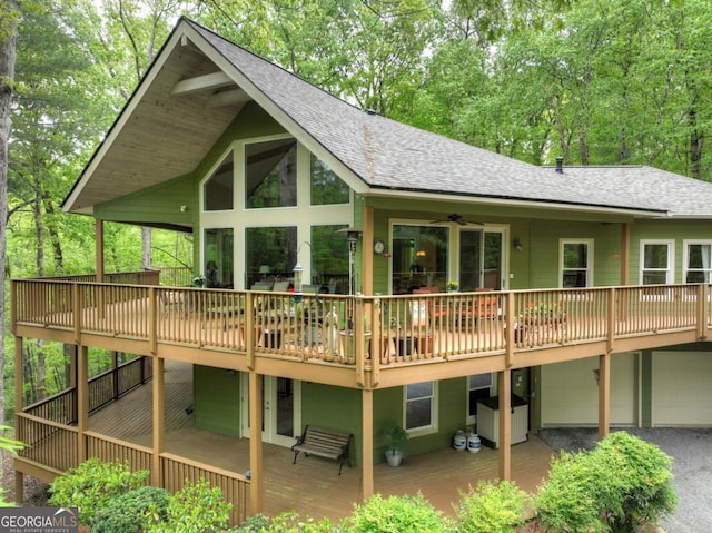 rear view of house with roof with shingles, a deck, an attached garage, and driveway