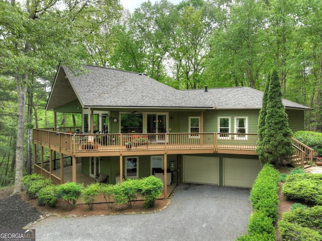 rear view of property with stairway, roof with shingles, an attached garage, a deck, and asphalt driveway