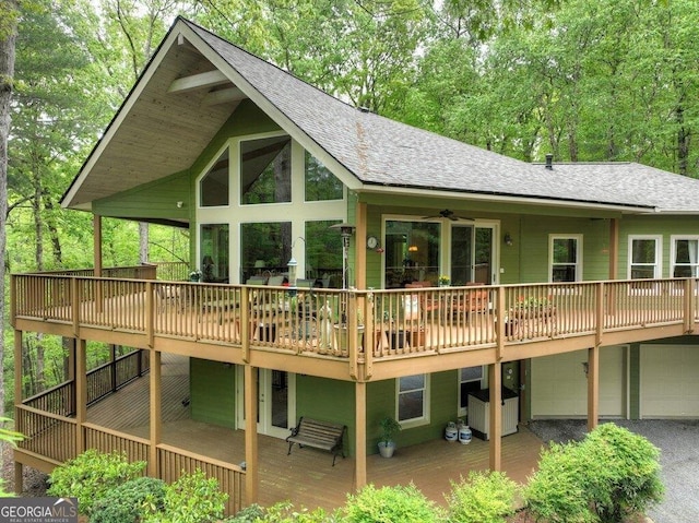 rear view of house with a shingled roof, a deck, and a garage