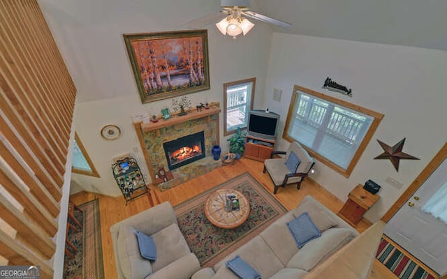 living area featuring a towering ceiling, wood finished floors, a stone fireplace, and ceiling fan