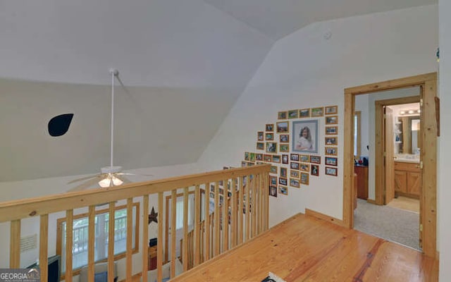 corridor featuring lofted ceiling, wood finished floors, and an upstairs landing