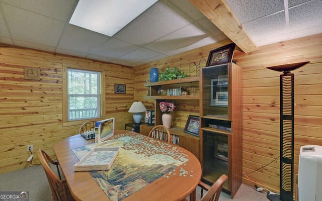 carpeted dining room with wooden walls and a paneled ceiling