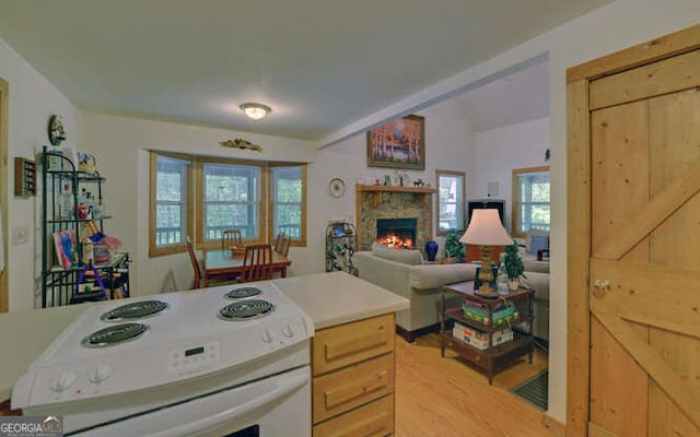 kitchen with white range with electric cooktop, light wood-style flooring, a stone fireplace, and plenty of natural light