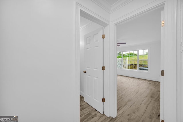 corridor with ornamental molding, light wood finished floors, and baseboards