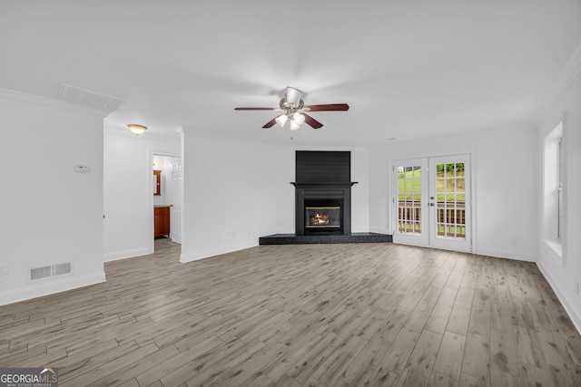 unfurnished living room with wood finished floors, ceiling fan, a fireplace, baseboards, and crown molding