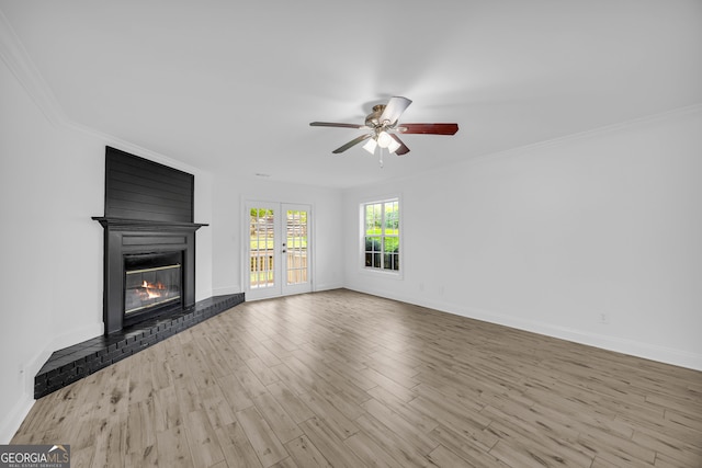 unfurnished living room with ceiling fan, a large fireplace, wood finished floors, baseboards, and crown molding