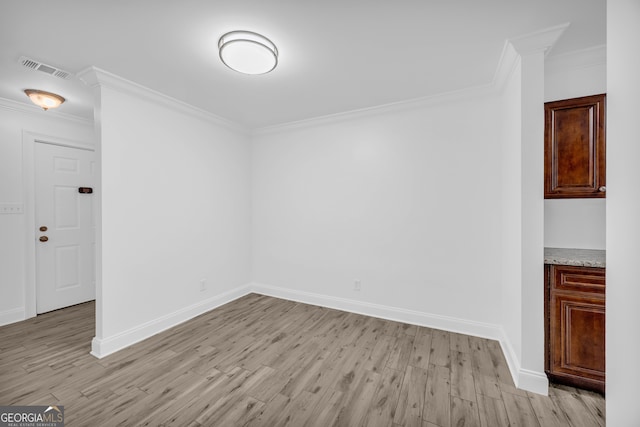 spare room featuring light wood finished floors, ornamental molding, and baseboards