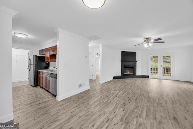 unfurnished living room with ceiling fan, a sink, light wood-style flooring, baseboards, and crown molding