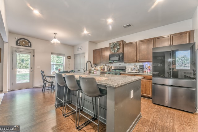 214 Willowbrook Way SE, Calhoun, GA 30701 - kitchen featuring appliances with stainless steel finishes, light wood-type flooring, a kitchen island with sink, a kitchen breakfast bar, and decorative backsplash