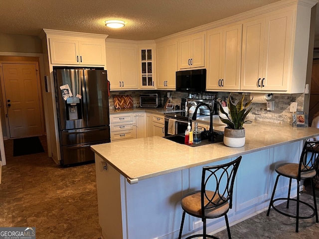 kitchen featuring fridge with ice dispenser, black microwave, a peninsula, white cabinets, and glass insert cabinets