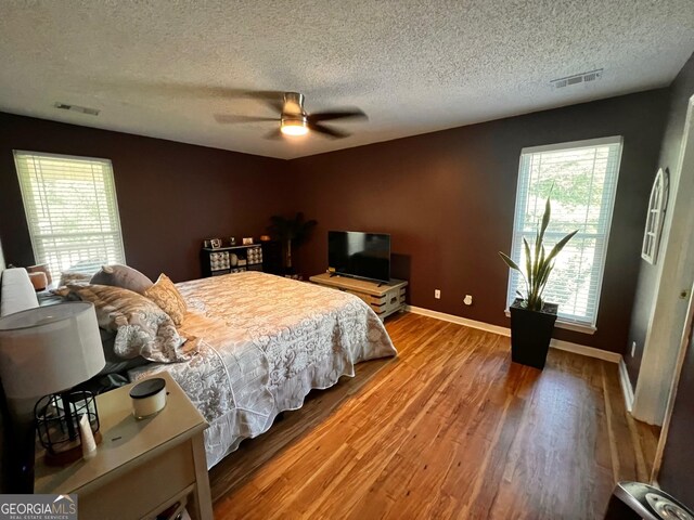 bedroom featuring a textured ceiling, wood finished floors, baseboards, and ceiling fan