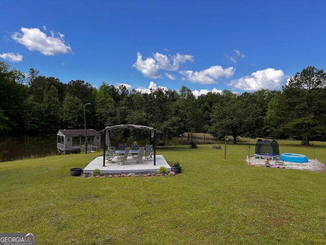 view of green lawn with a patio area, a gazebo, a trampoline, and a wooded view