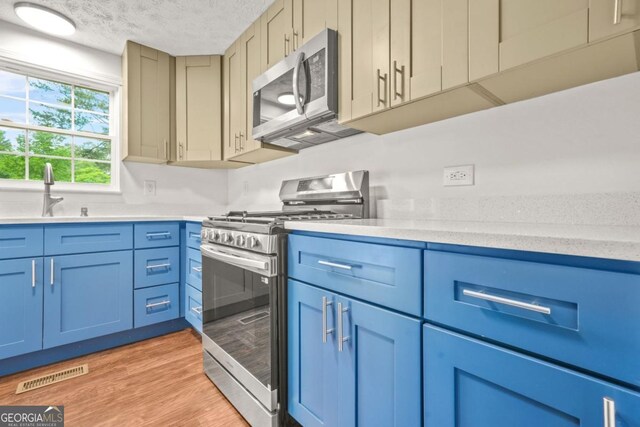 1355 Tucker Woods Dr, Norcross, GA 30093 - kitchen featuring appliances with stainless steel finishes, a sink, blue cabinets, a textured ceiling, and light wood finished floors