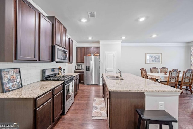 kitchen featuring stainless steel appliances, crown molding, a kitchen breakfast bar, decorative backsplash, and an island with sink