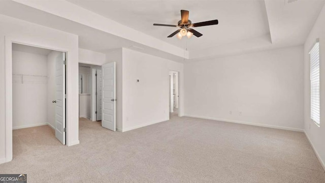 unfurnished bedroom with light carpet, a raised ceiling, baseboards, and a spacious closet