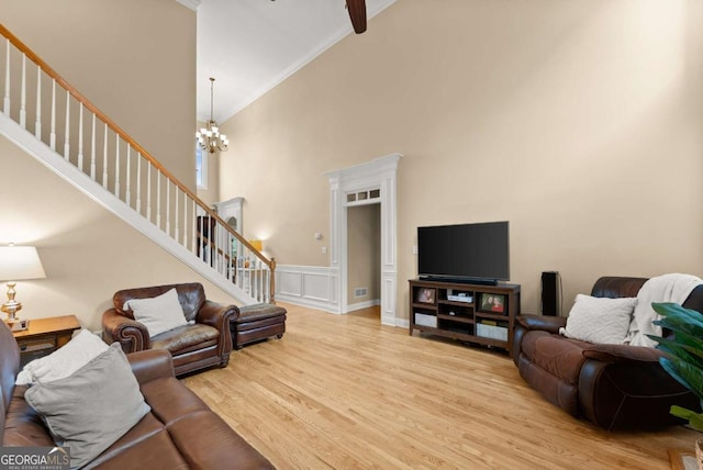 living area with stairway, a chandelier, ornamental molding, light wood finished floors, and a high ceiling