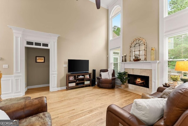 living room with a fireplace, a towering ceiling, healthy amount of natural light, wood finished floors, and crown molding