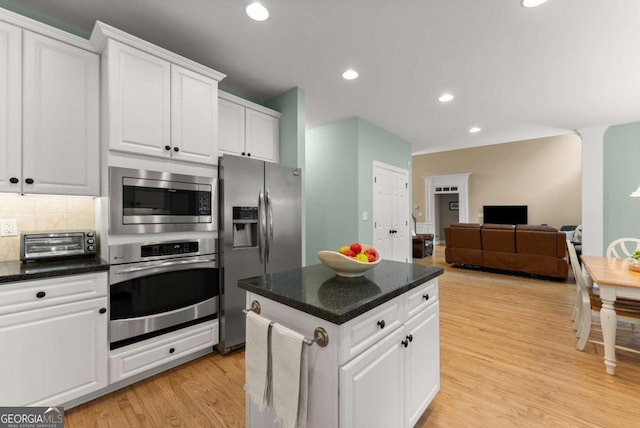 kitchen featuring stainless steel appliances, white cabinets, backsplash, light wood-style floors, and open floor plan