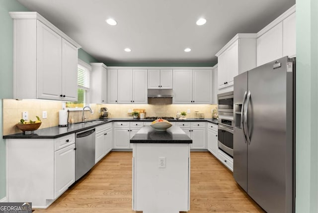 kitchen with stainless steel appliances, a sink, a center island, under cabinet range hood, and white cabinetry
